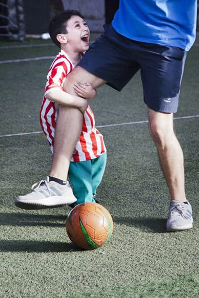 alumno motrinfan divertido agarrándole la pierna al profe mientras juegan a la pelota