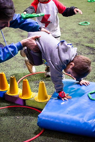 profesor ayudando a alumno a pararse de cabeza sobre una colchoneta